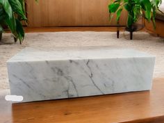 a white marble box sitting on top of a wooden table next to a potted plant