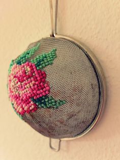 a needle - embroidered rose is hanging on the wall next to a metal rack with it's handle