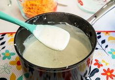 a spoon in a pot filled with liquid on top of a colorful place mat and table cloth