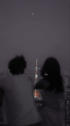 two people are looking at the moon in the night sky over a cityscape