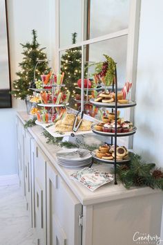 an assortment of desserts and pastries on a buffet table with christmas trees in the background