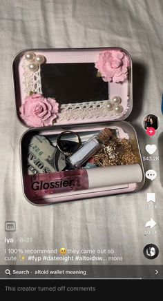 an open tin with some items inside of it on a bed next to a cell phone