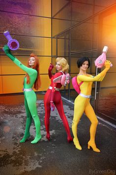 three barbie dolls are standing in front of a building with an orange and yellow background