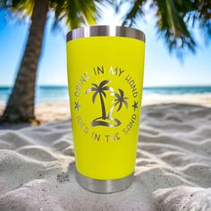 a yellow cup sitting on top of a sandy beach next to the ocean and palm trees