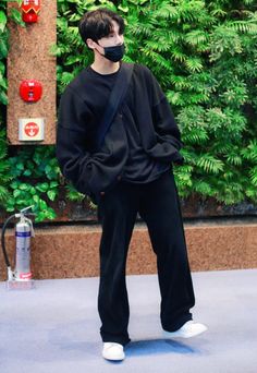 a man wearing a face mask while standing in front of a wall with green plants