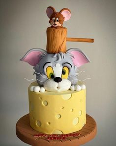 a cake decorated with an image of a mouse on top of a cheese slice and a wooden stick sticking out of it