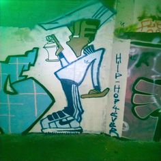 some graffiti on the side of a wall with green and blue colors, including one person holding a skateboard