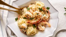 a white plate topped with pasta and shrimp next to a fork on a tablecloth