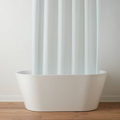 a white tub sitting on top of a hard wood floor next to a wall with a shower curtain