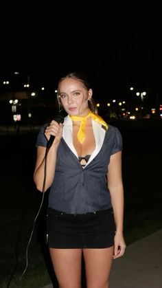 a woman standing on the sidewalk holding a microphone in her hand and wearing a tie around her neck