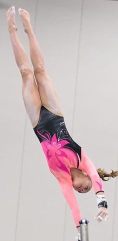 a woman on the balance beam doing a handstand in an indoor gymnastics arena