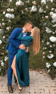 a man in a blue suit kissing a woman's face with flowers behind them