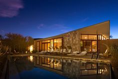 an outdoor swimming pool at night with lounge chairs and lights on the patio area next to it