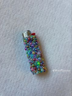 a cell phone covered in beads on top of a white surface with a red button