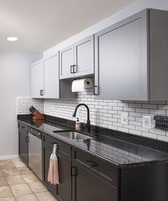 a kitchen with gray cabinets and black counter tops, white subway tile backsplash