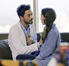 a man and woman sitting on a couch talking to each other in front of a window