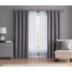 a living room with grey curtains and a white chair in front of a window that is open