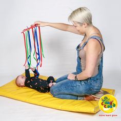 a woman playing with a baby on a mat