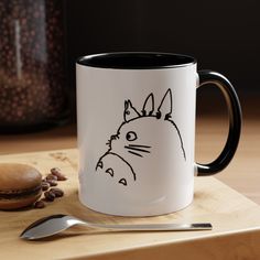 a coffee mug with a drawing of totoro on it next to a spoon