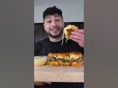 a man is holding up a sandwich with meat and cheese on it while sitting at a table