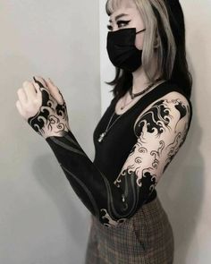 a woman with black and white tattoos on her arm wearing a face mask covering her mouth