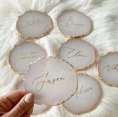 six personalized glass coasters with gold lettering on white furnishing, one being held up by a person's hand