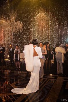 a woman in a long white dress standing next to a man wearing a fur coat