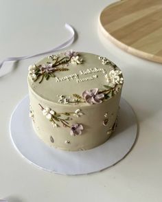 a white cake with flowers on it sitting on a plate next to a wooden cutting board