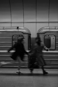 two people are walking past a train in black and white