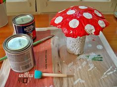 a red mushroom sitting on top of a table next to paint cans and a brush