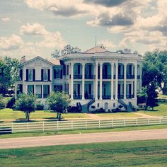 a large white house sitting on top of a lush green field next to a road