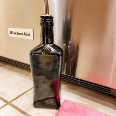 a black bottle sitting on the floor next to a pink towel and a stainless steel dishwasher