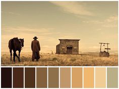 a man standing next to a horse on top of a dry grass field in front of an old building