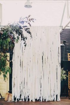 a white curtain hanging from the ceiling in front of a plant and potted tree