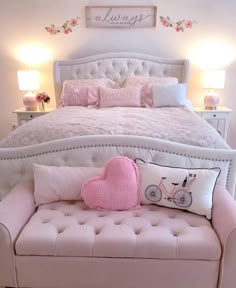 a white bed with pink pillows and a heart pillow on the footboard next to it