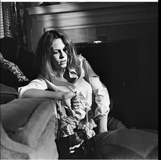 a black and white photo of a woman sitting on a couch with her arm around a pillow