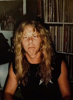 a man with long hair sitting in front of a book shelf filled with books and records