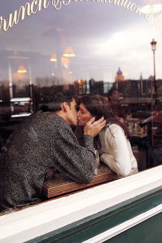 a man and woman kissing in front of a window