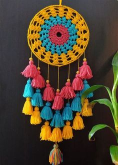 a crocheted doily with tassels hanging on a wall next to a potted plant