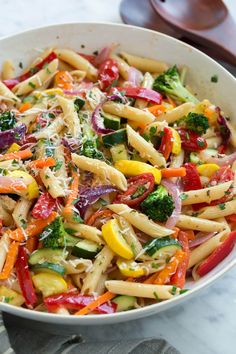 a bowl filled with pasta and veggies on top of a marble countertop