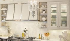 a kitchen with white cabinets and marble counter tops, an oven hood over the stove is lit by a crystal chandelier