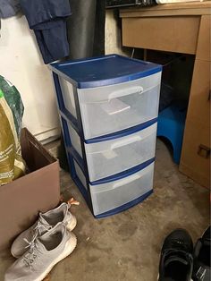 a pair of shoes sitting on the floor next to a blue and white box with three drawers