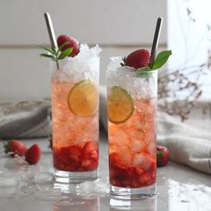 two glasses filled with ice and strawberries on top of a white table next to each other