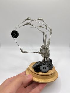 a hand holding a small metal sculpture with buttons on it's sides and a wire spider attached to the base