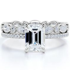 an emerald cut diamond ring set with white diamonds on the band and side stones around it