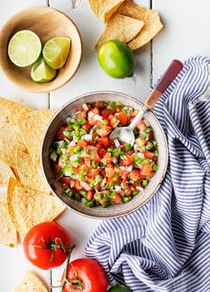 a bowl filled with salsa surrounded by tortilla chips, tomatoes and limes