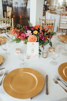 the table is set with gold plates, silverware and floral centerpieces for an elegant wedding reception