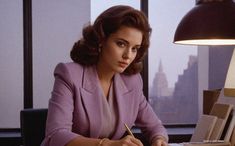 a woman sitting at a desk with a pen and paper in her hand, writing