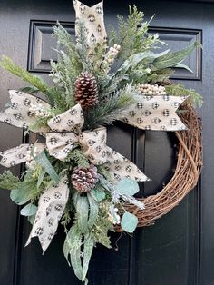 a wreath with pine cones and greenery is hanging on the front door's black door