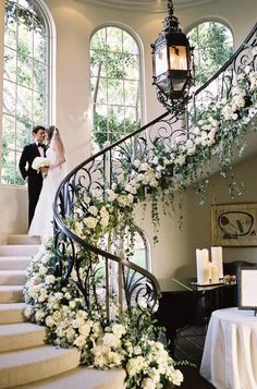 a bride and groom are standing on the stairs next to each other with flowers in front of them